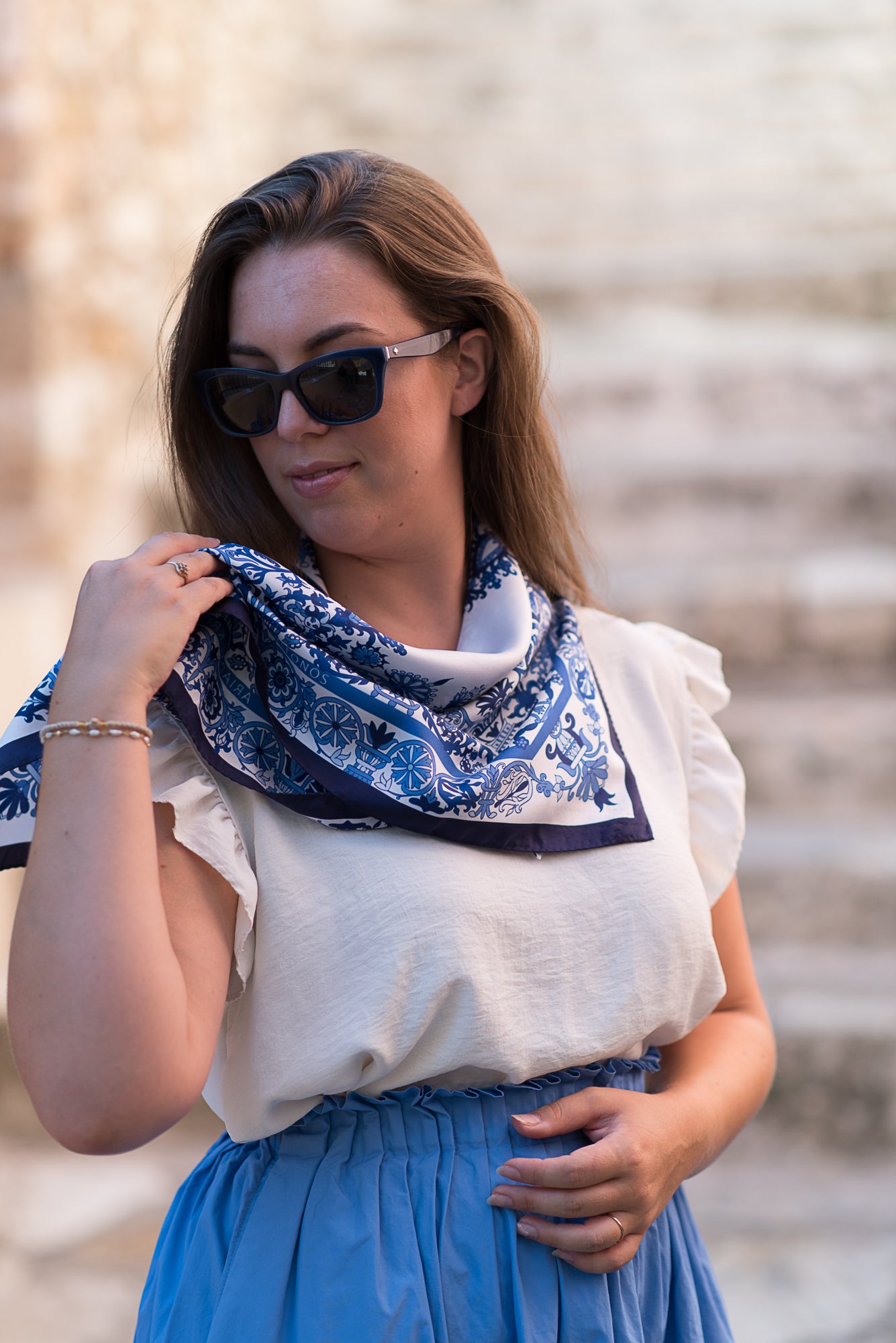Woman wearing a blue and white scarf with designs from Cretan embroidery, sunglasses, and a white top with a blue skirt.